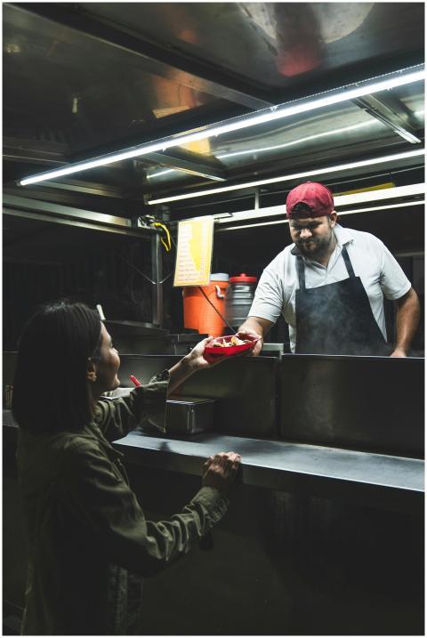 A street food vendor hands a taco to a customer at