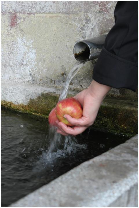 A person washes a red apple under a flowing water