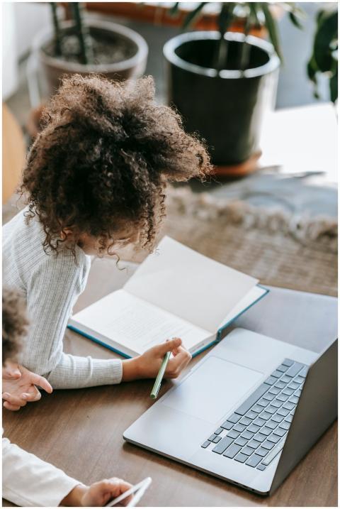Young girl focusing on homework using a laptop, in