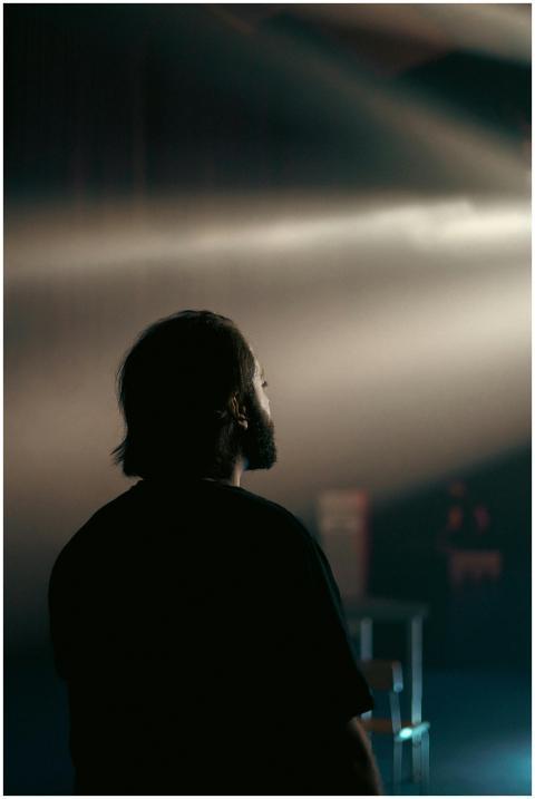A man with black hair and beard stands under conce