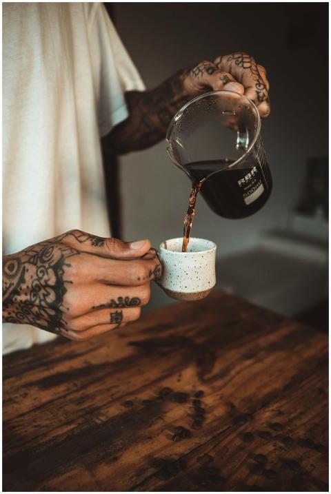A tattooed barista pouring freshly brewed coffee i