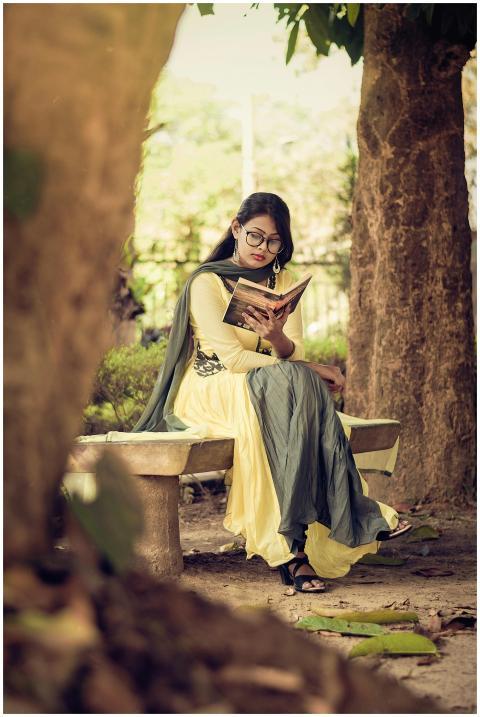 South Asian woman reading a book on a bench in a s