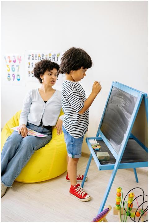 A young boy writes on a blackboard with a teacher