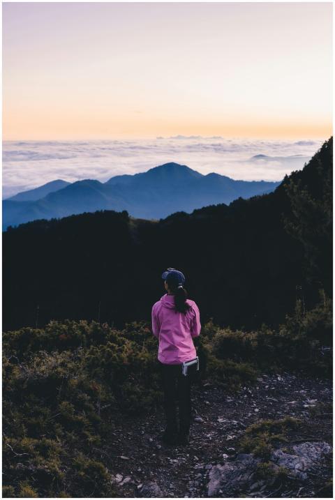 A woman in a pink jacket stands on a mountain path