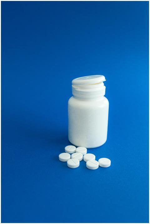 White pill bottle with scattered tablets on blue s
