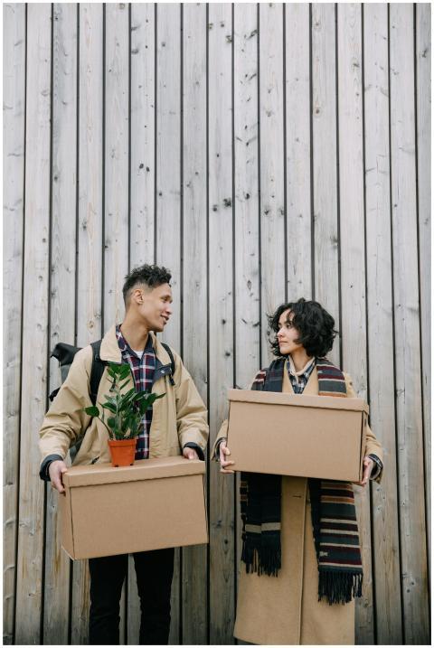 A couple carrying cardboard boxes with a plant, st