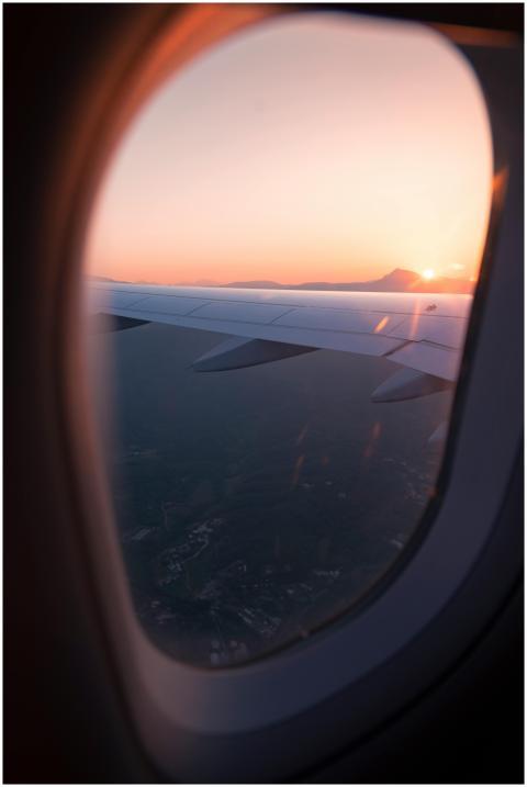 Airplane wing view through window during sunset, c