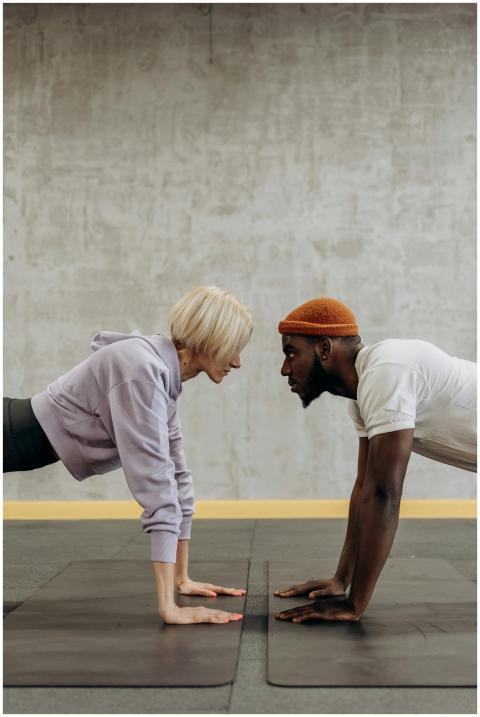 Two adults face off in a plank exercise on gym mat