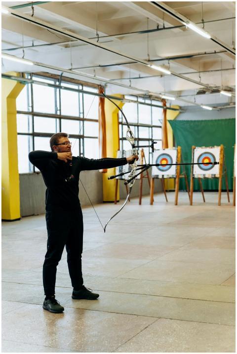 A man practicing archery indoors, aiming at a bull