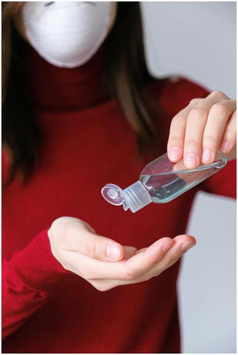 A woman in a red sweater applies hand sanitizer in
