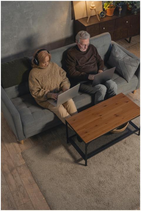 Elderly couple sitting on a sofa, using laptops fo