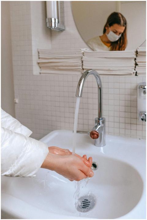 Woman wearing a face mask washing hands in a clean