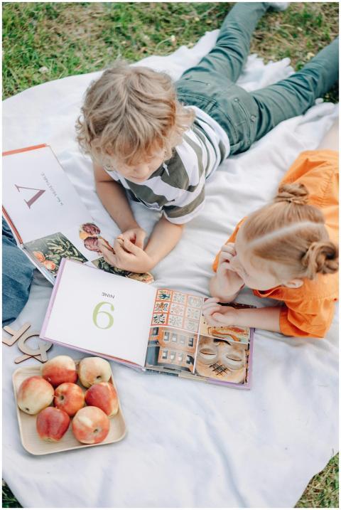 Two children reading books on a picnic blanket wit