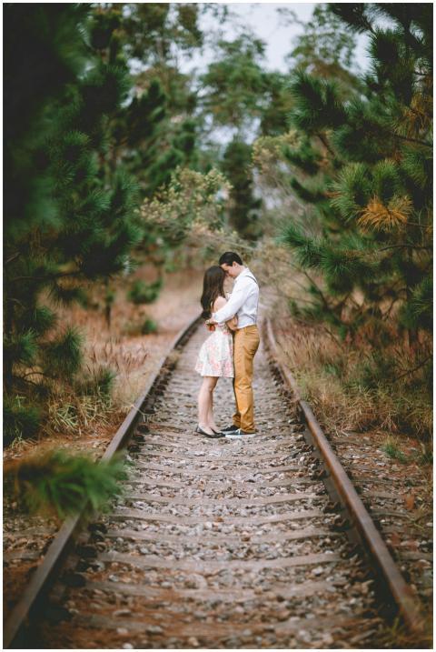 A romantic couple embracing on railway tracks surr