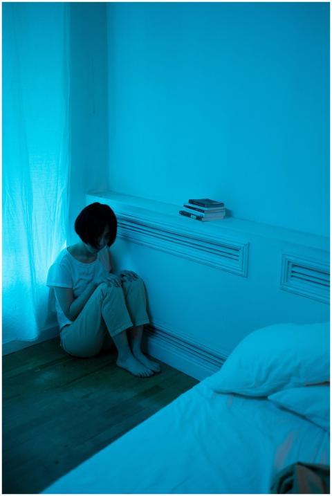 A woman sits alone in a blue-lit room, conveying a