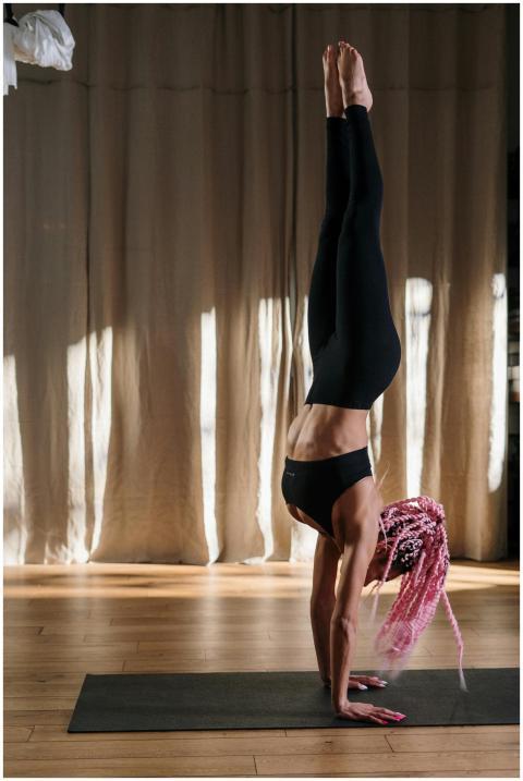 A woman with pink hair practices a handstand on a