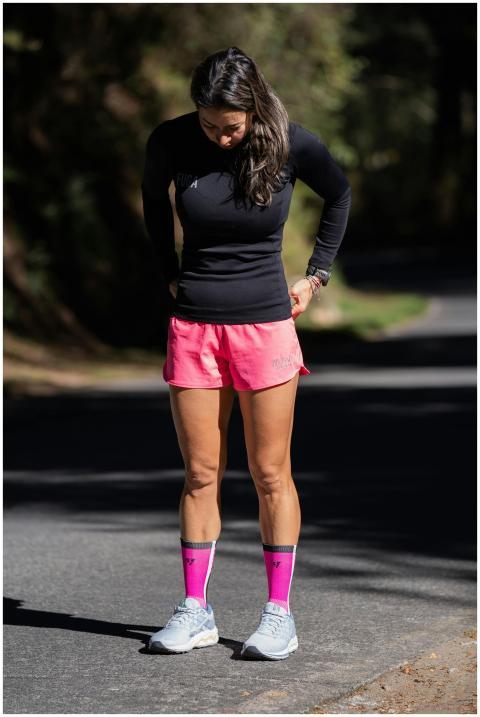 A female jogger pausing on a shaded path wearing b