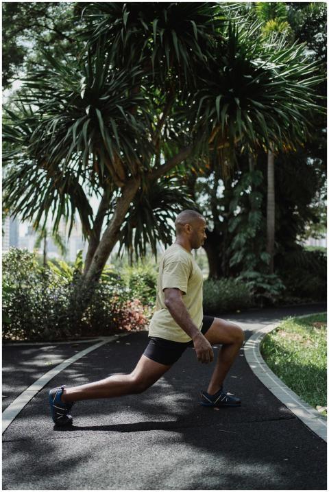 A black man performing lunges on a path in a lush