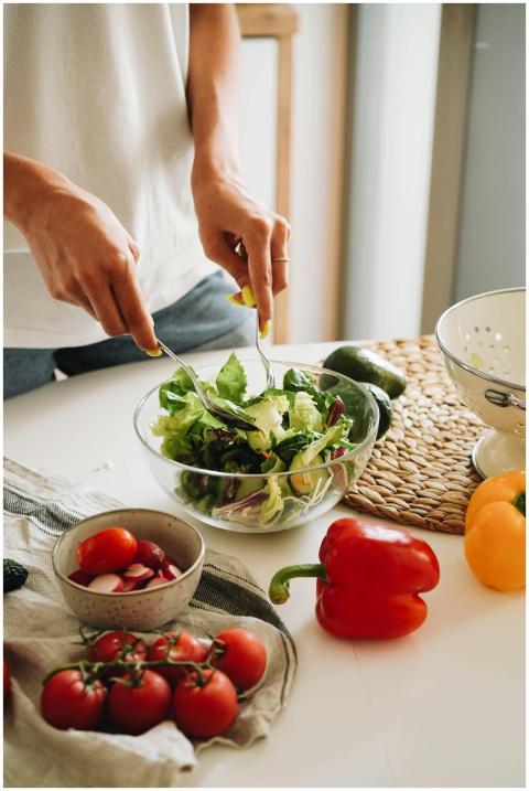 A person mixes a fresh vegetable salad with tomato