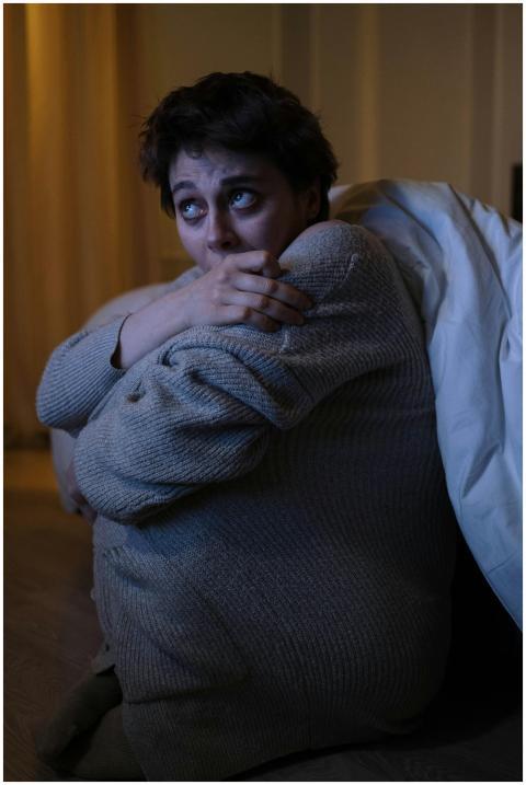Anxious woman sitting alone in dimly lit room, dep