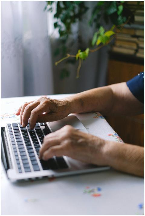 Elderly person typing on a laptop indoors, showing