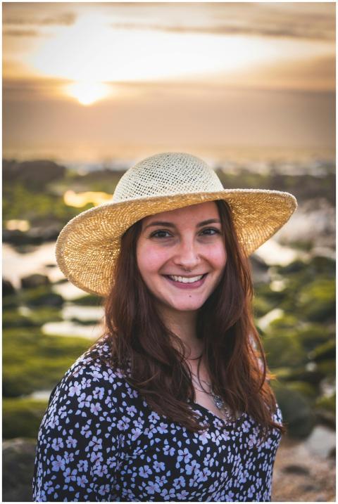 A joyful woman wearing a straw hat enjoys a sunset