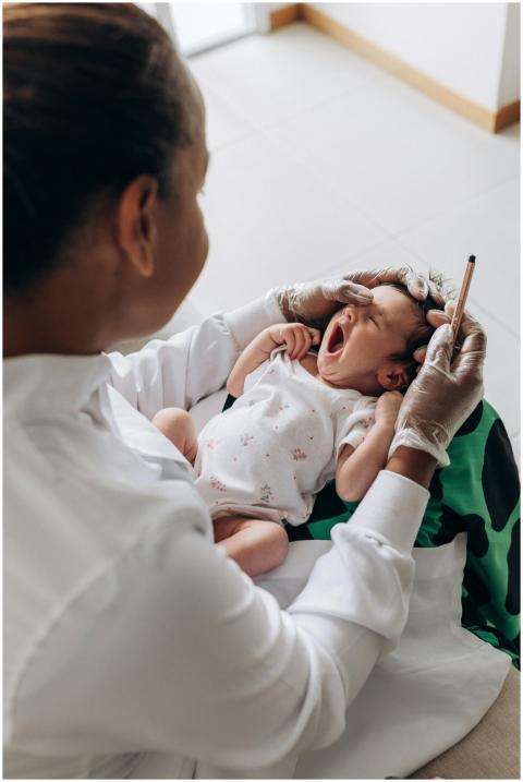 A newborn baby yawns during a health checkup by a