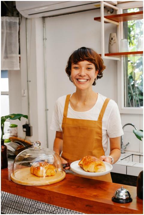 Charming waitress in apron serving croissant with