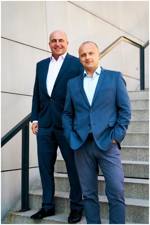 Two businessmen in suits confidently pose on an ou