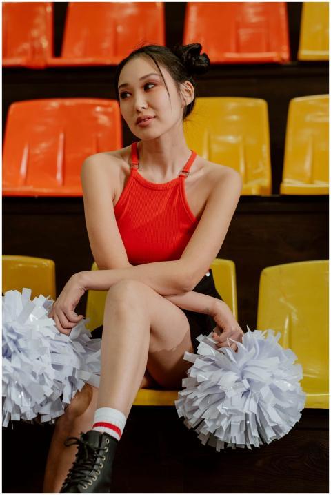 Asian woman cheerleader in orange top and black sk