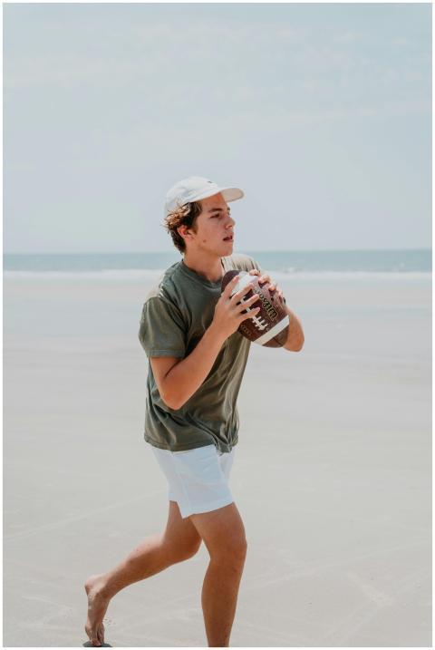 Teen wearing a cap playing football on a sunny bea