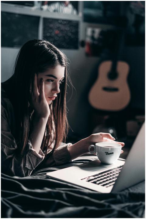 Woman lying on bed, focused on laptop with a coffe