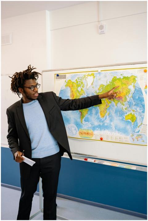 Man teaching geography, pointing at a world map, s