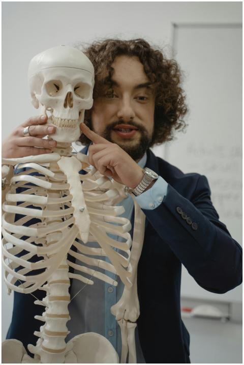 Male teacher in a suit explains a human skeleton m