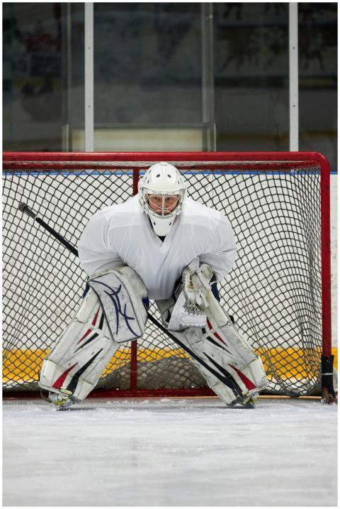 A hockey goalie in white gear guards the net on an