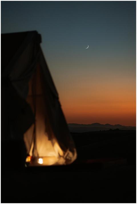A glowing tent at dusk under a crescent moon in Pa