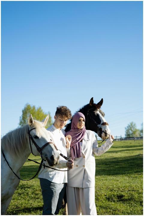 Couple standing together with horses on a sunny da