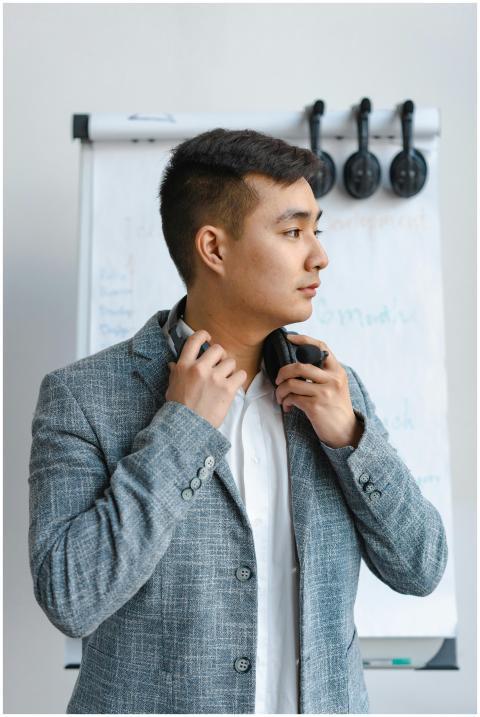 Asian man standing indoors with headphones, wearin