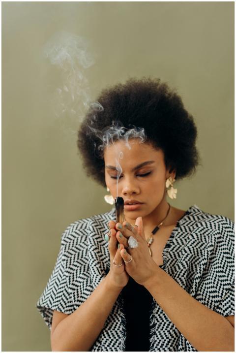 A woman meditates indoors, focusing on incense smo