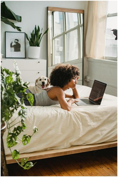 Woman with curly hair using laptop on bed with dog