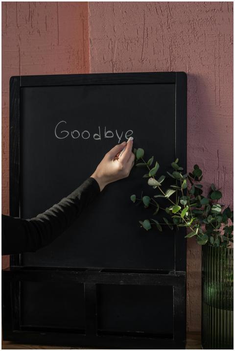 A hand writes 'Goodbye' on a chalkboard, indoors,