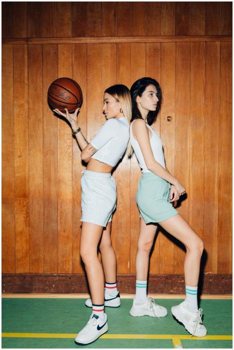 Two female athletes pose with basketball in gym. S