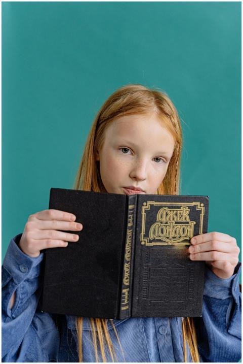 A young girl holds a book, posing against a solid