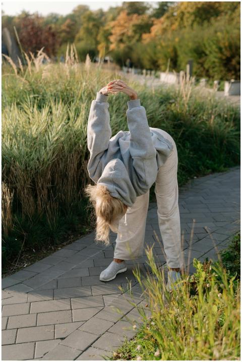 Woman in a hoodie stretching in a park on a sunny