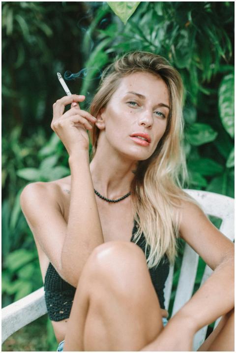 Blonde woman sits in garden holding cigarette, ser