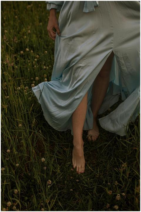 A woman in a flowing blue dress walks barefoot thr