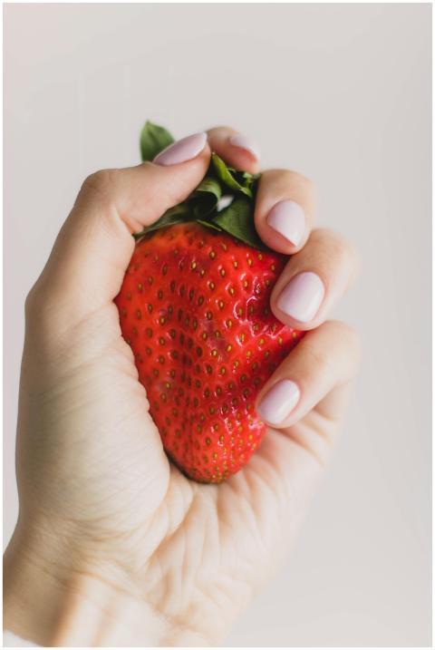 A close-up image of a hand grasping a ripe red str