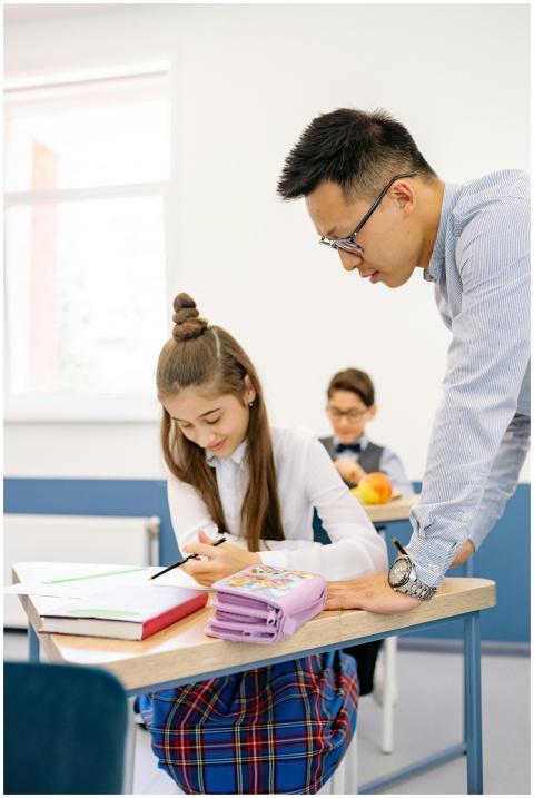 A teacher helps a student at her desk in a bright