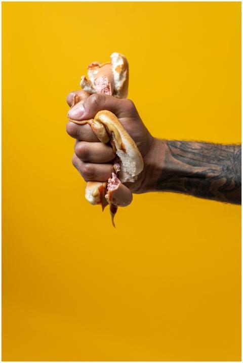 Close-up of a tattooed hand squeezing a hotdog, em