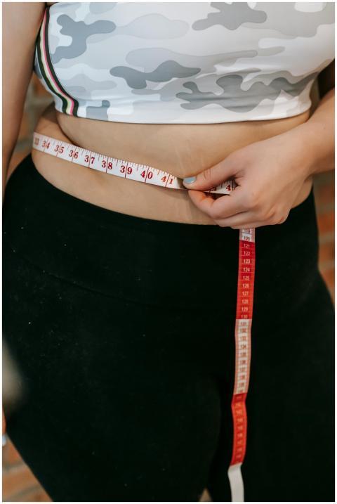 A woman measures her waist using a red measuring t